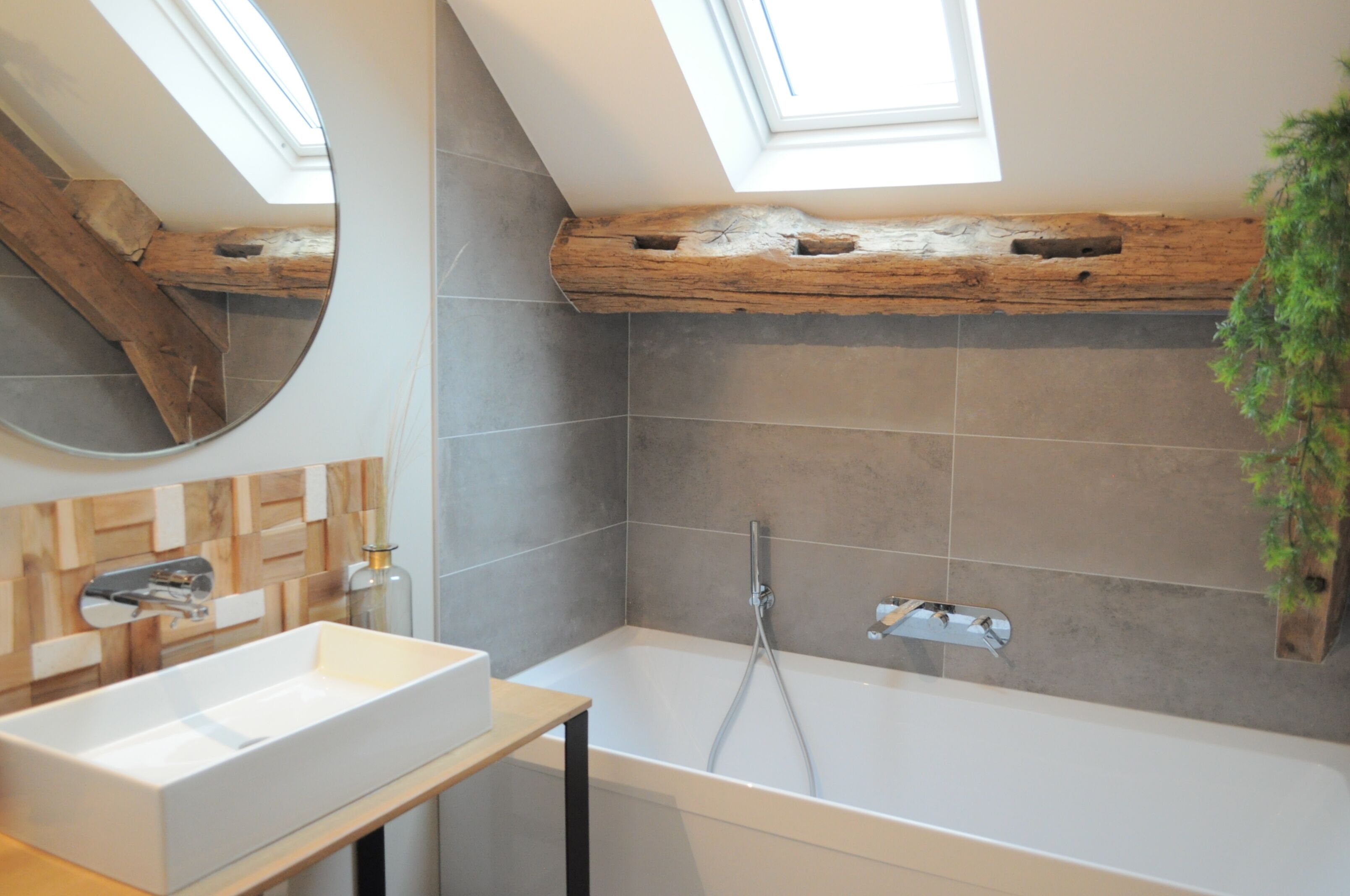 A modern bathroom with a skylight, a wooden beam ceiling, a large bathtub, and a white sink.