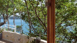 Tranquila zona de estar al aire libre con un banco de madera y una estatua de Buda, rodeada de exuberante vegetación y con vistas a un cuerpo de agua.
