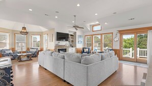 Un salon spacieux avec un grand canapé d’angle gris, un plancher en bois et un ventilateur de plafond.