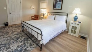 Een slaapkamer met een bed, een stoel, een nachtkastje met een lamp en een deur.