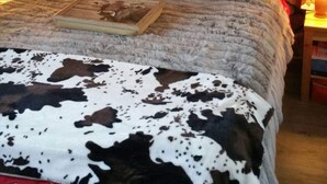 A cozy bedroom with a stone wall, a cow-patterned blanket, and red polka-dotted pillows. - Chaleureux Appartement (Ancelle)