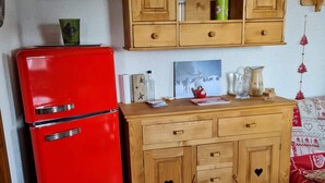 A kitchen with a red refrigerator, wooden cabinets, and a tiled floor. - Chaleureux Appartement (Ancelle)