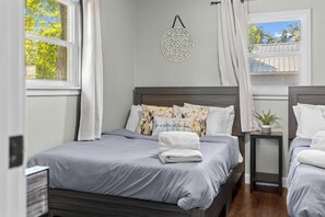 A bedroom with a bed, bedside tables, a wall decor, and windows. - Cozy cottage walk to parks near lake and downtown (Coeur d'Alene)
