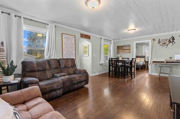 A spacious living area with a brown leather sofa, a dining table with chairs, and a kitchen area.