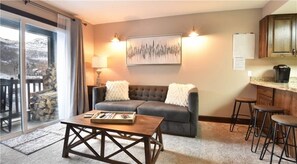 A cozy living room with a sofa, a coffee table, and a dining area with stools. - 1BD PowderPointe Condo-Walk to Resort! (Park City)