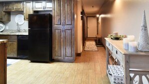 Una cuina amb armaris de fusta, un refrigerador negre i una zona de menjador amb taula i cadires.