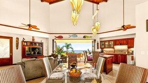 A spacious living area with a large dining table, comfortable seating, a television, and a kitchen with wooden cabinets.