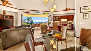 A spacious living area with a sofa, dining table, and chairs, a kitchen with wooden cabinets, and a view of the ocean.