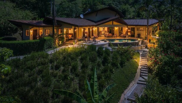 A two-story house with a swimming pool, surrounded by lush greenery and a night sky.