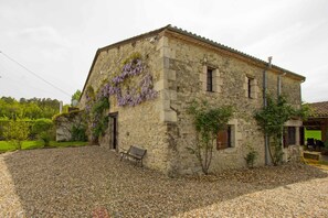 A stone building with a gravel driveway, a bench, and a pergola with purple vines. - Stone house with a heated pool, views, big garden. Short drive to historic towns (Lévignac-de-Guyenne)