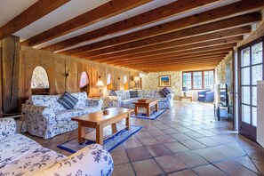 A spacious living area with wooden beams, stone walls, and a large window.