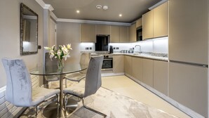 A modern kitchen with a glass dining table, grey upholstered chairs, and beige cabinetry. - Bootham Urban Space -  a family break that sleeps 4 guests  in 2 bedrooms (York)