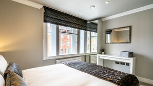 A bedroom with a large bed, a bedside table, a mirror, and a window with a view of buildings. - Bootham Urban Space -  a family break that sleeps 4 guests  in 2 bedrooms (York)