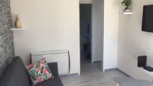 Un salon moderne avec un canapé gris, une petite table et un téléviseur fixé au mur.