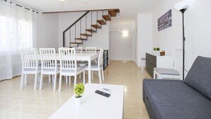 A modern living room with a grey sofa, white dining table, and chairs. A staircase with wooden steps leads to another room. - Villa  ADELFA (Salou)