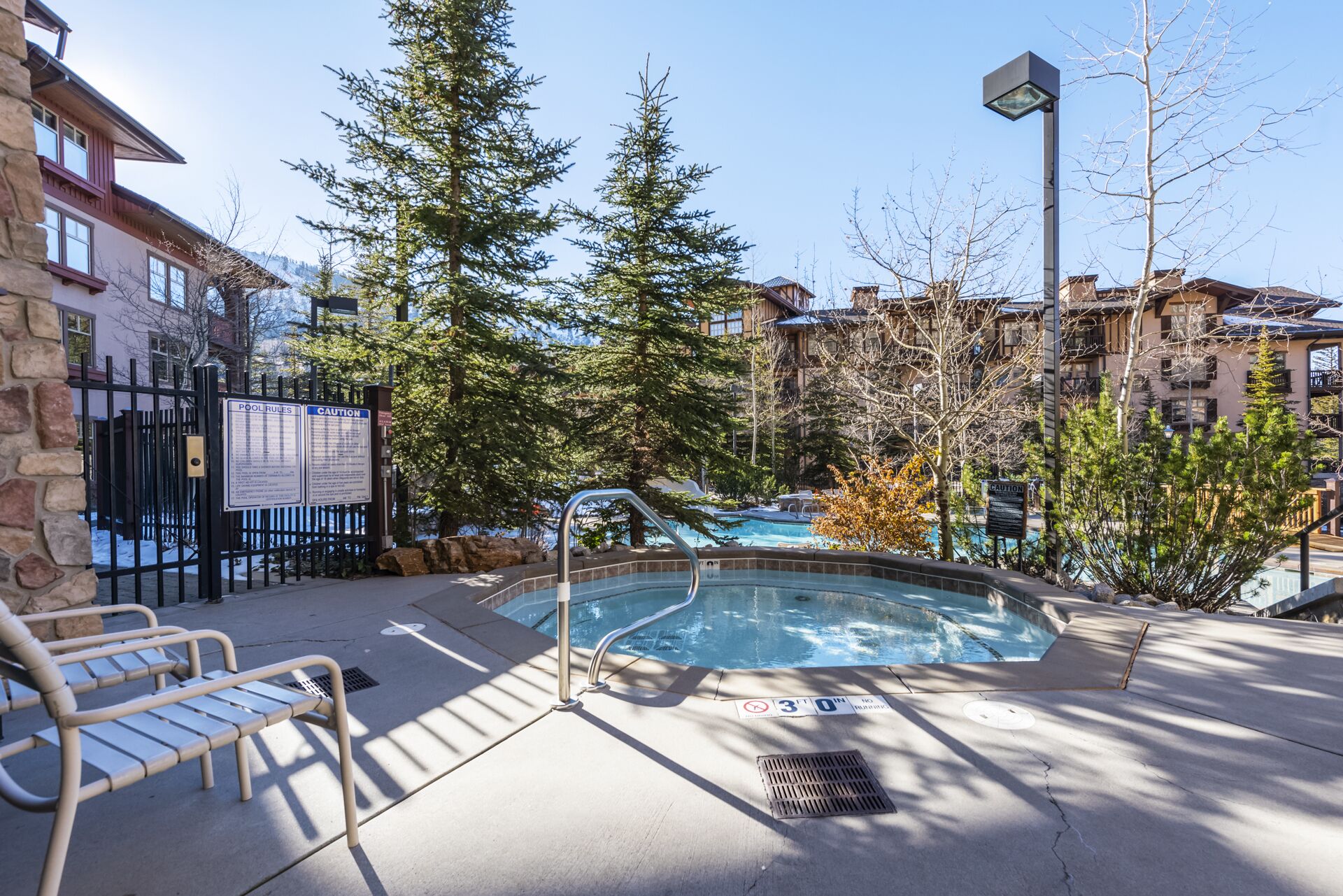 Un espace piscine comprenant un jacuzzi, des chaises longues et un panneau indiquant les règles à respecter au bord de la piscine.
