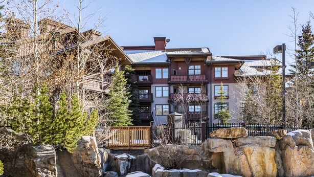 Un hotel de varios pisos con balcones, un jardín de rocas y nieve en el suelo.