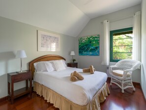 A bedroom with a wooden bed, a nightstand, a chair, a window with curtains, and a painting on the wall.