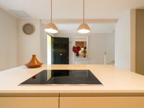 A kitchen with a black induction cooktop, a white countertop, a wall clock, and pendant lights.
