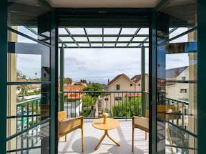 En balkon med to fletstole og et lille rundt bord, med udsigt over et boligområde med huse og grønt.
