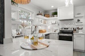 A modern kitchen with white cabinetry, a central island with a bottle and glasses, and a hanging light fixture.