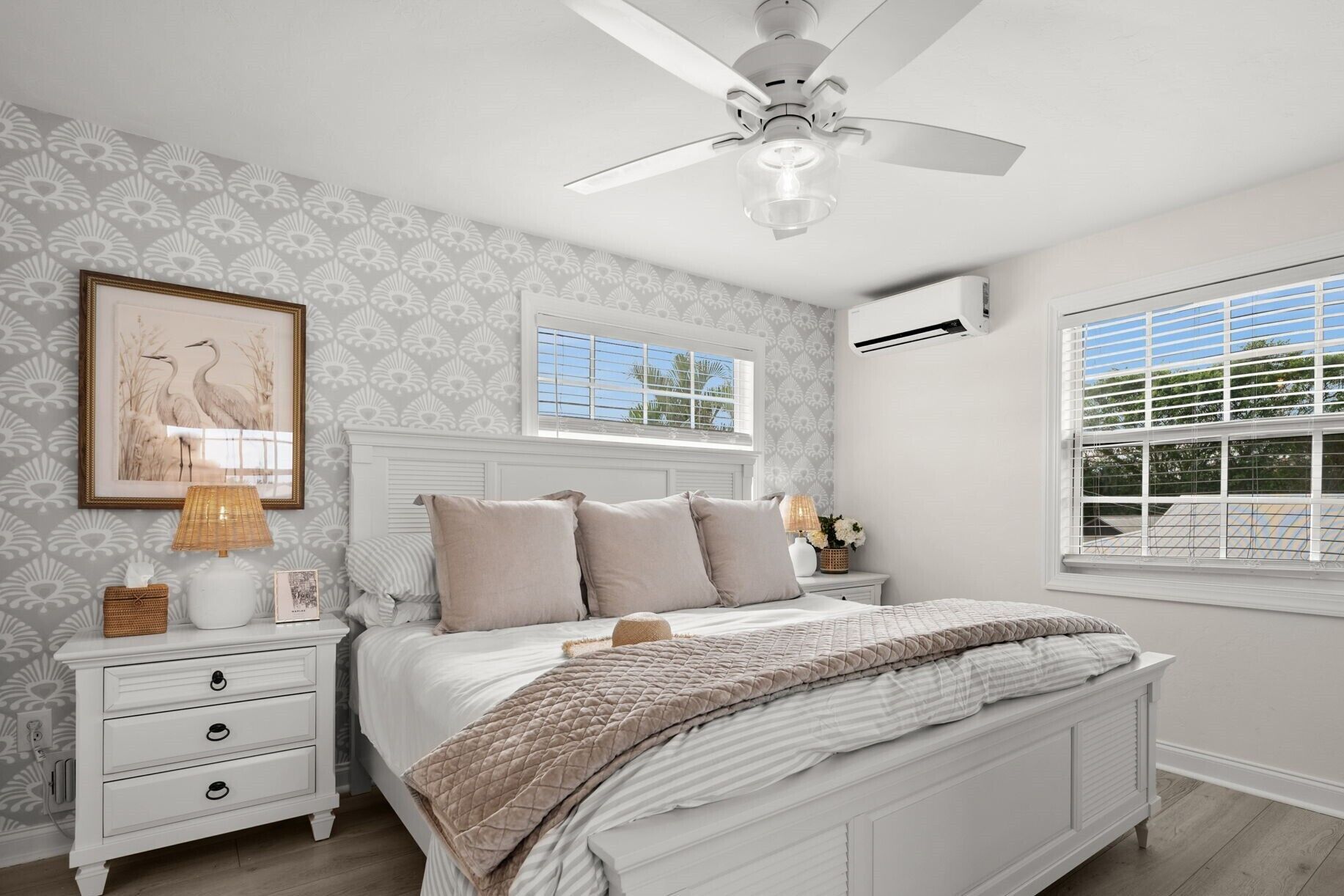 A bedroom with a bed, nightstands, a ceiling fan, and two windows.