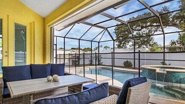 Eine sonnendurchflutete Terrasse mit Glasveranda, Korbmöbeln und einem Pool.