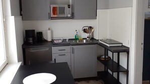 Ett kompakt kök med ett svart bord, grå skåp, en mikrovågsugn, en kaffebryggare och ett handfat.
