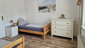 Ett sovrum med en säng i trä, en vit byrå, ett nattduksbord, en lampa och en tavla som föreställer en strandvy.