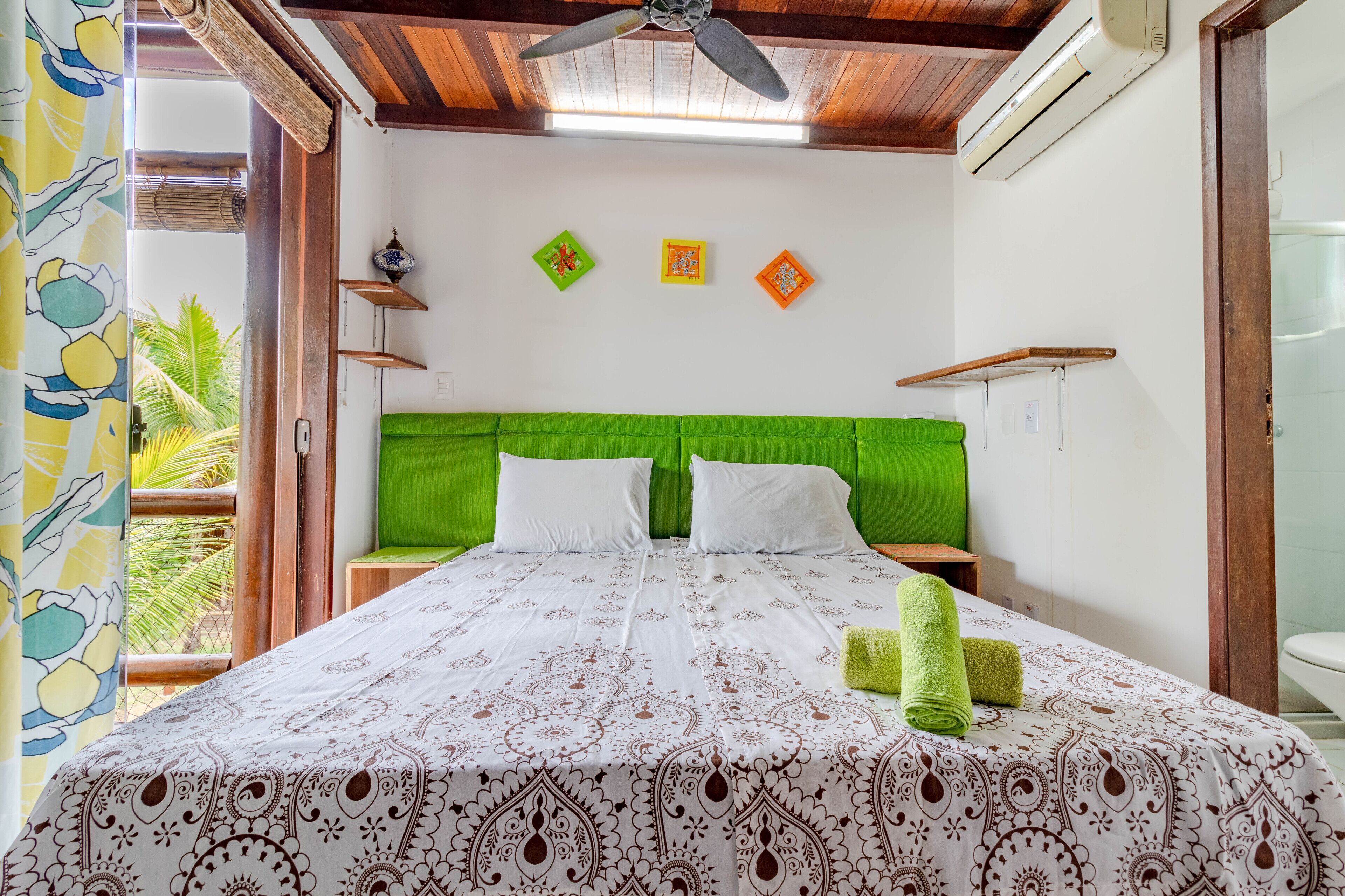 Une chambre avec un lit, une tête de lit verte et un ventilateur de plafond.
