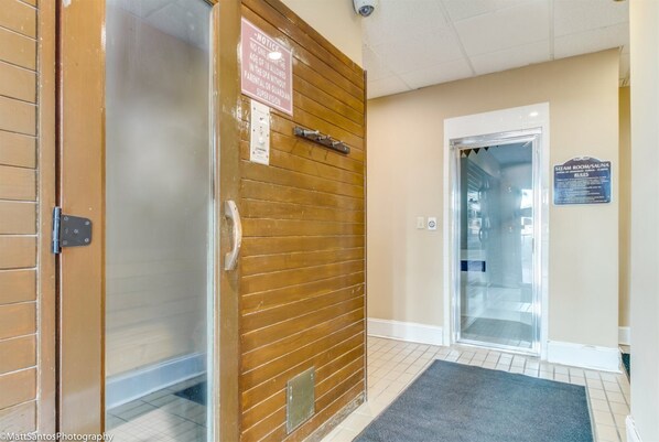 A hotel entrance with a wooden door, a glass door leading to a steam room/saloon, and a sign indicating no one under 18 allowed without supervision. - Palace Resort 2212 (Myrtle Beach)