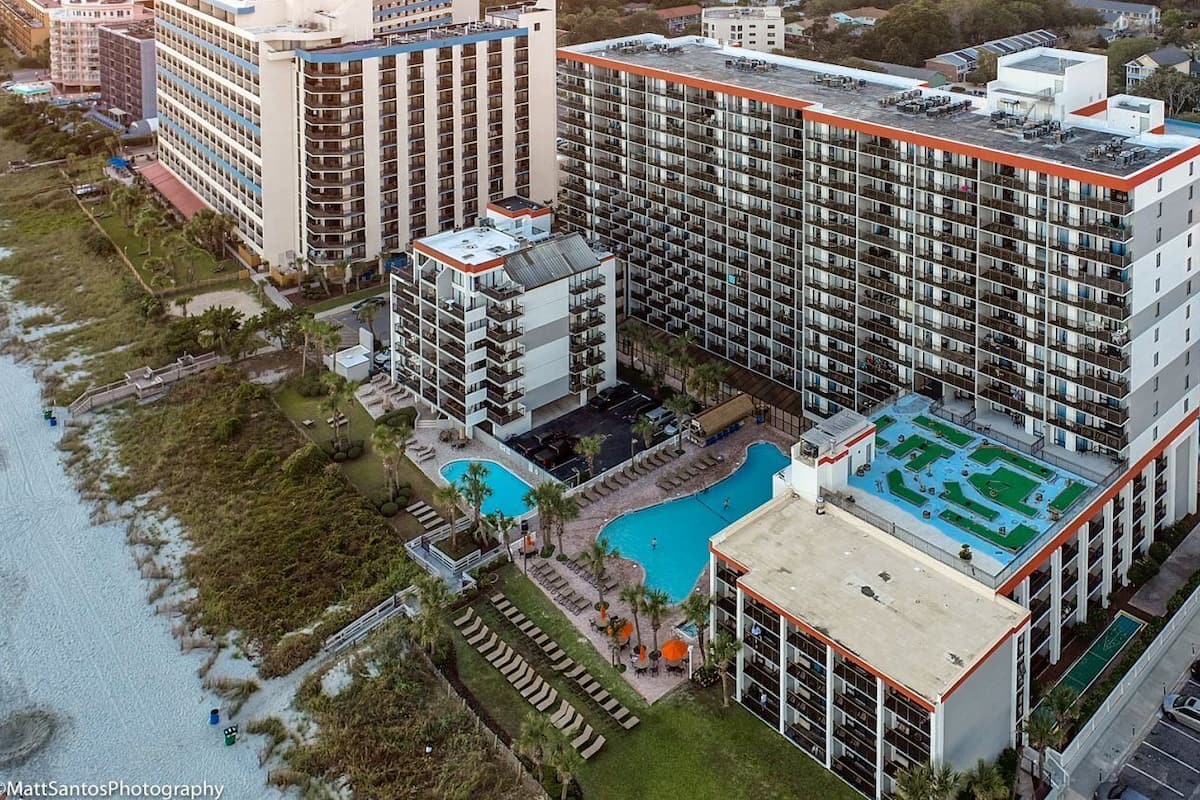 A high-rise hotel with multiple floors, a rooftop pool, and a landscaped pool area.