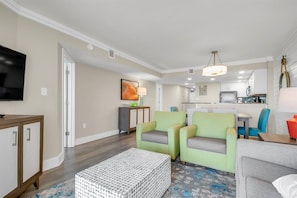 A modern living room with a flat-screen TV, a coffee table, and two green armchairs.