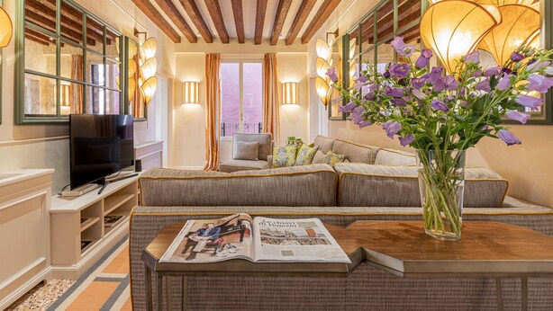 A modern living room with a sofa, a coffee table with a magazine, a TV, and a vase with flowers. - L'Opera Divina (Venice)