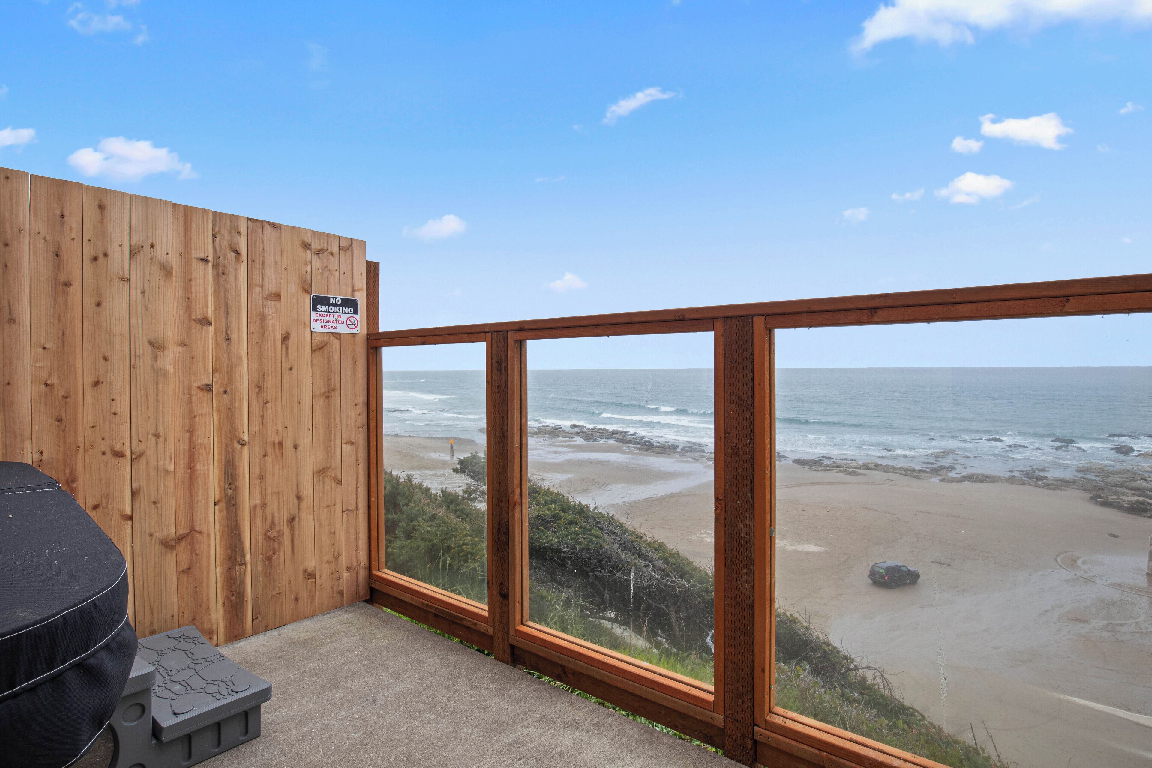 Un balcon en bois donnant sur une plage, avec un panneau indiquant qu'il est interdit de fumer.