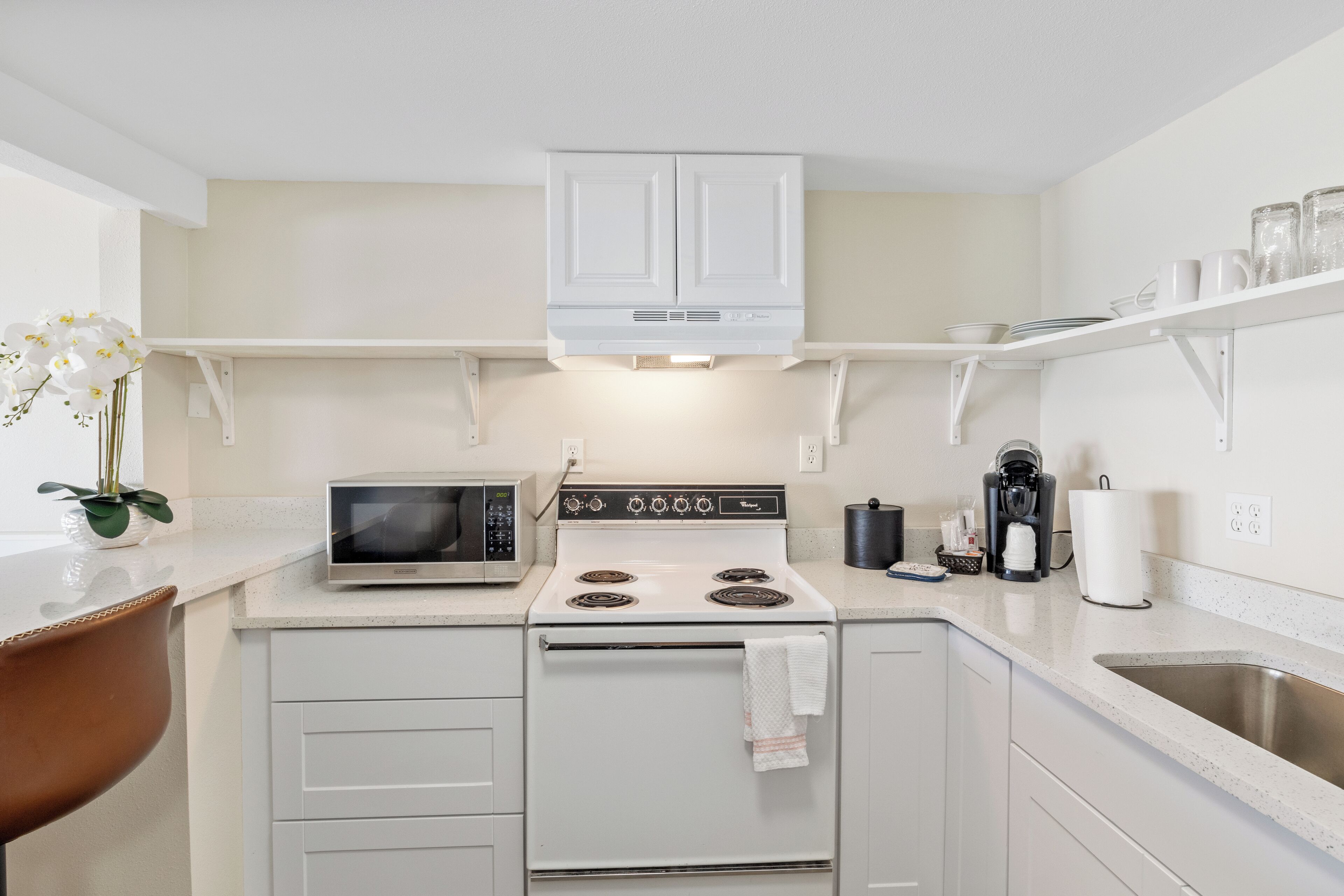 A compact kitchen with white cabinets, a microwave, stove, and a coffee maker.