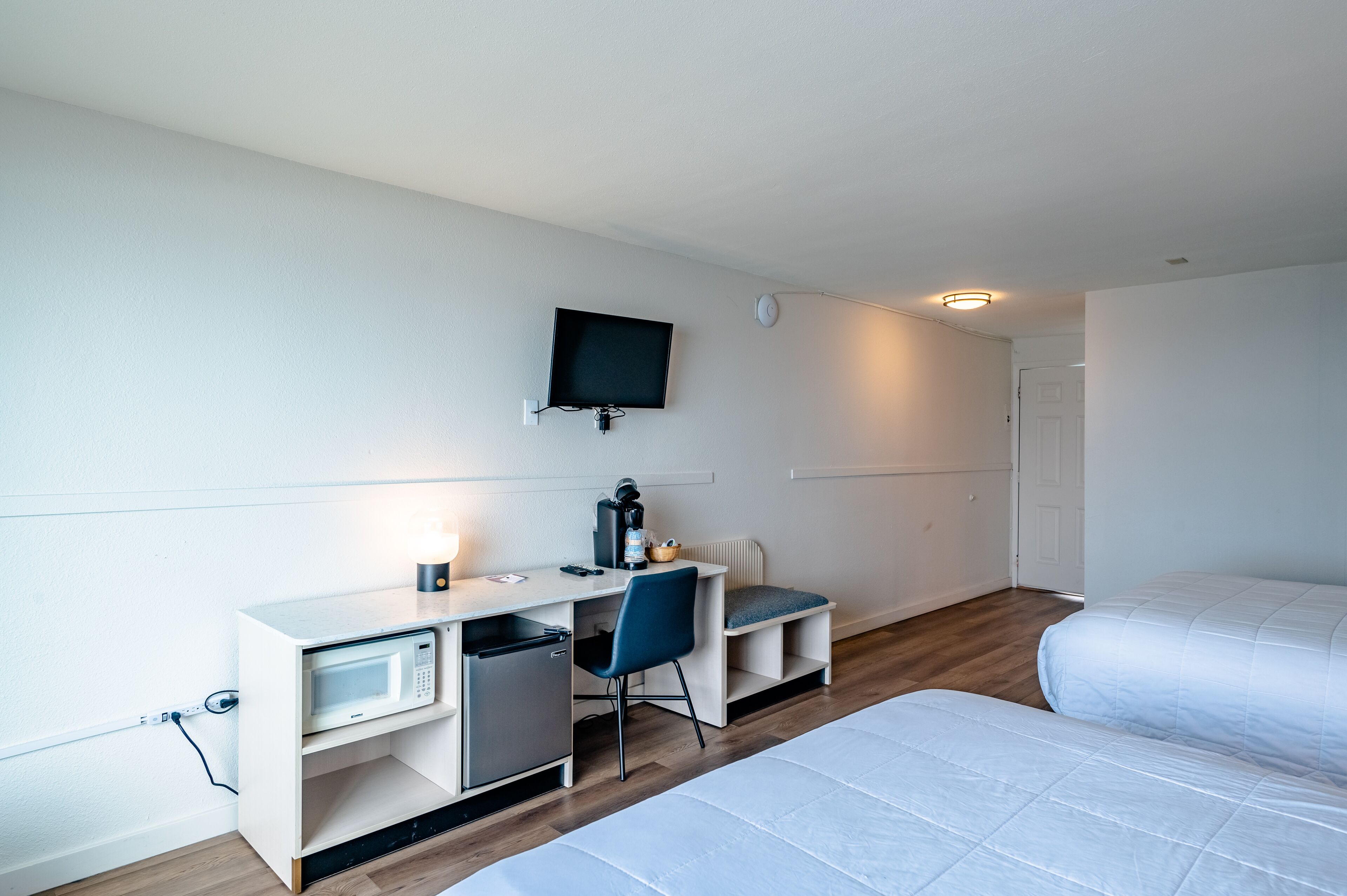 Una habitación de hotel compacta con kitchenette, una cama individual y un televisor fijado a la pared.
