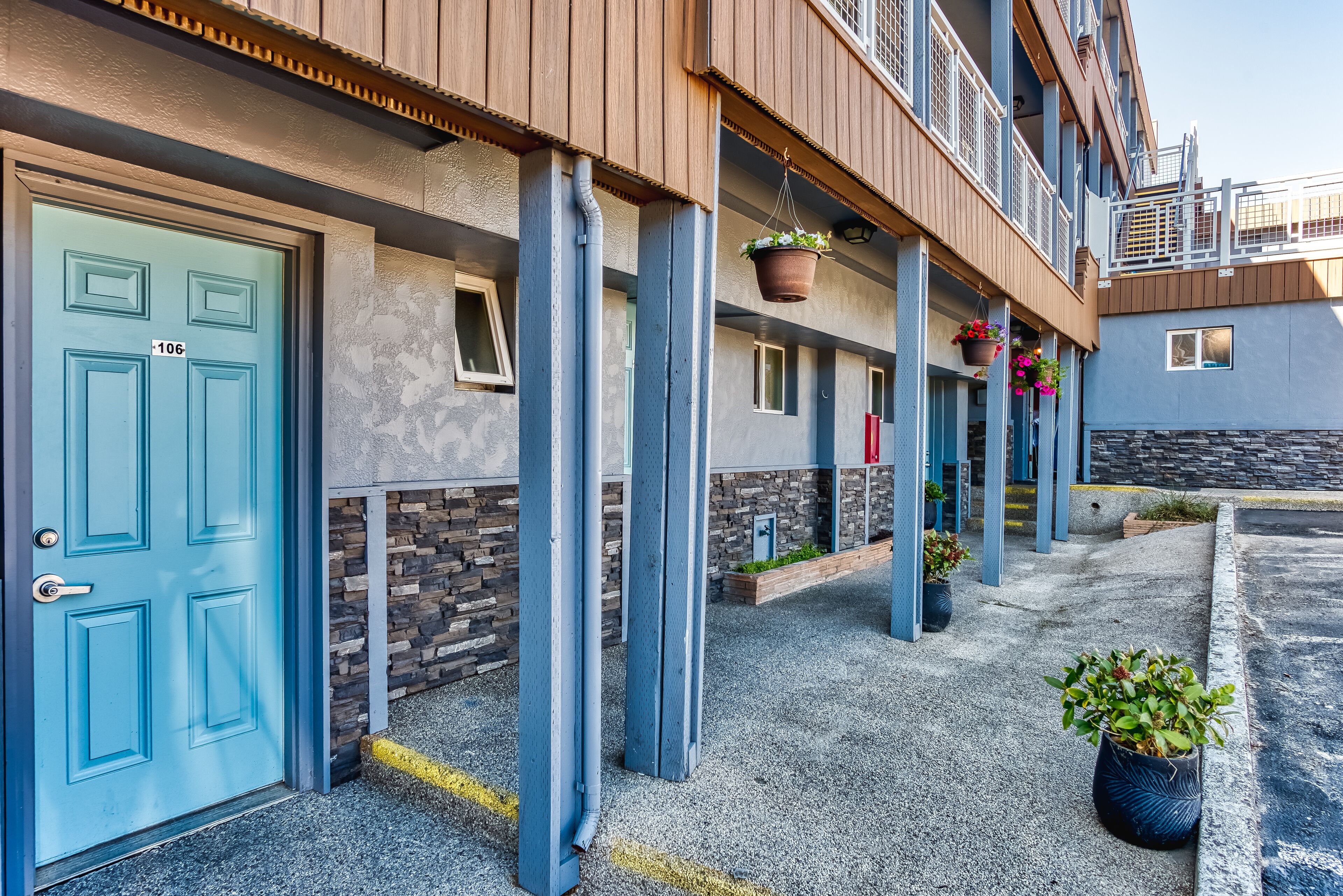 A building with a blue door marked "106", outdoor potted plants, and a stone wall.