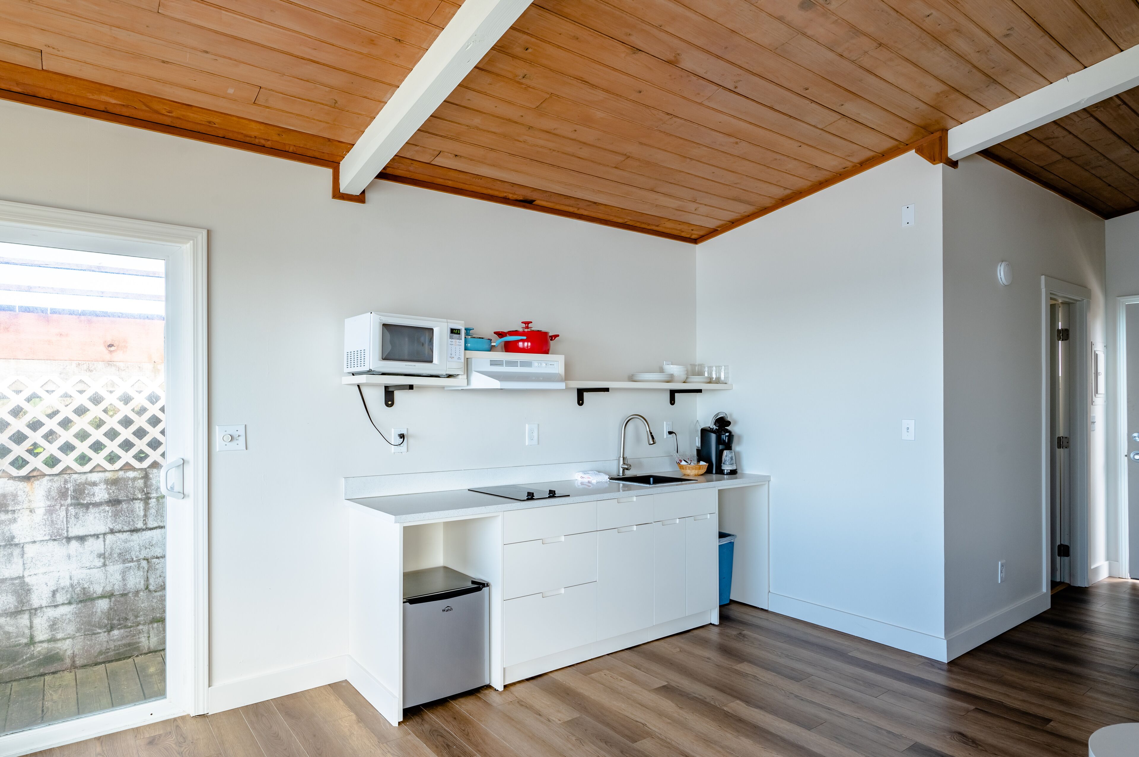 A modern kitchen with white cabinetry, a microwave, a red pot, and a sink.