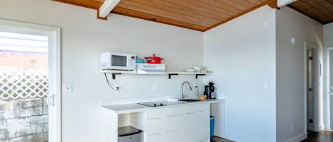 A modern kitchen with white cabinetry, a microwave, a red pot, and a sink.