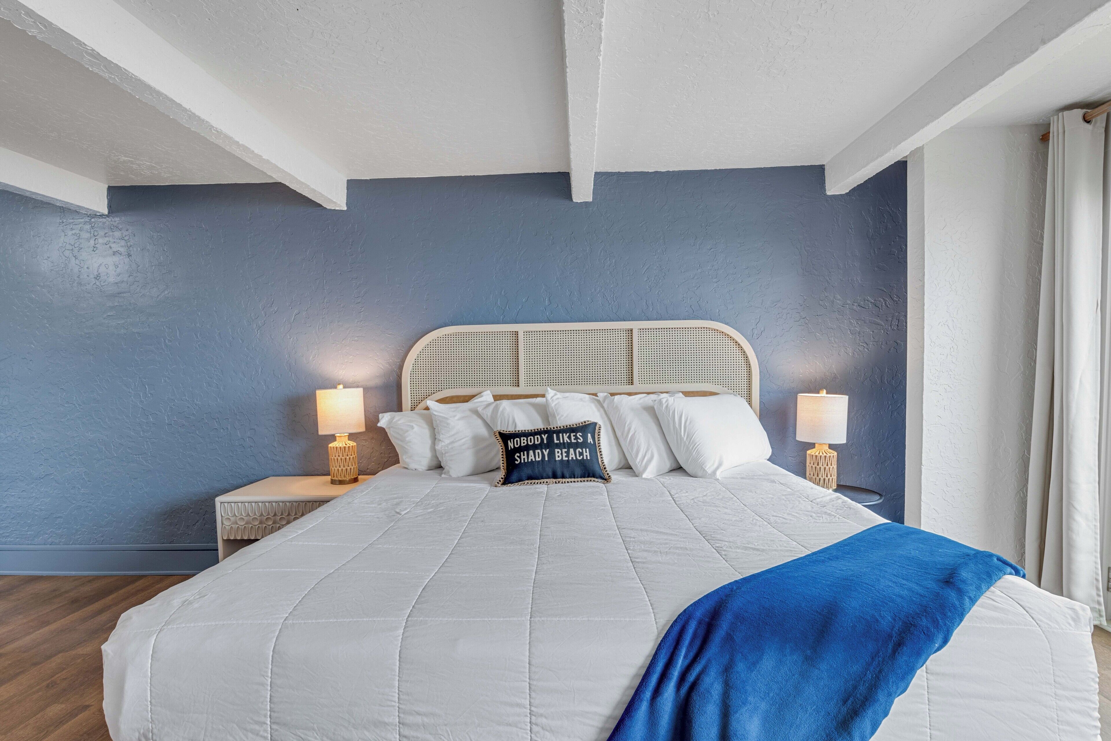 A bedroom with a large bed, two bedside tables with lamps, and a wall with a textured blue paint.
