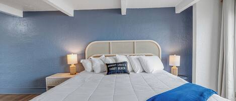 A bedroom with a large bed, two bedside tables with lamps, and a wall with a textured blue paint.
