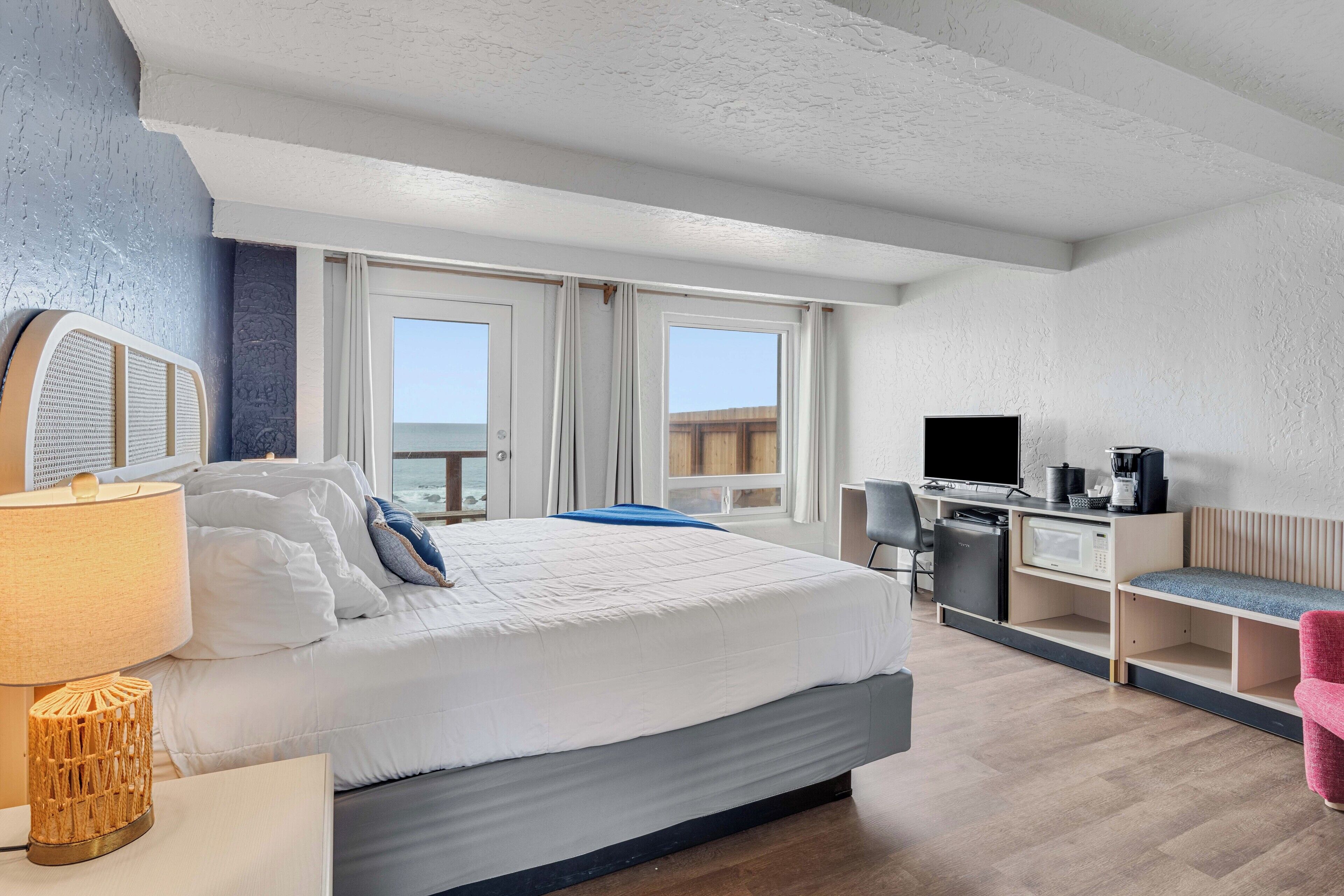 A modern hotel room with a large bed, a desk, a television, and a balcony with a view.