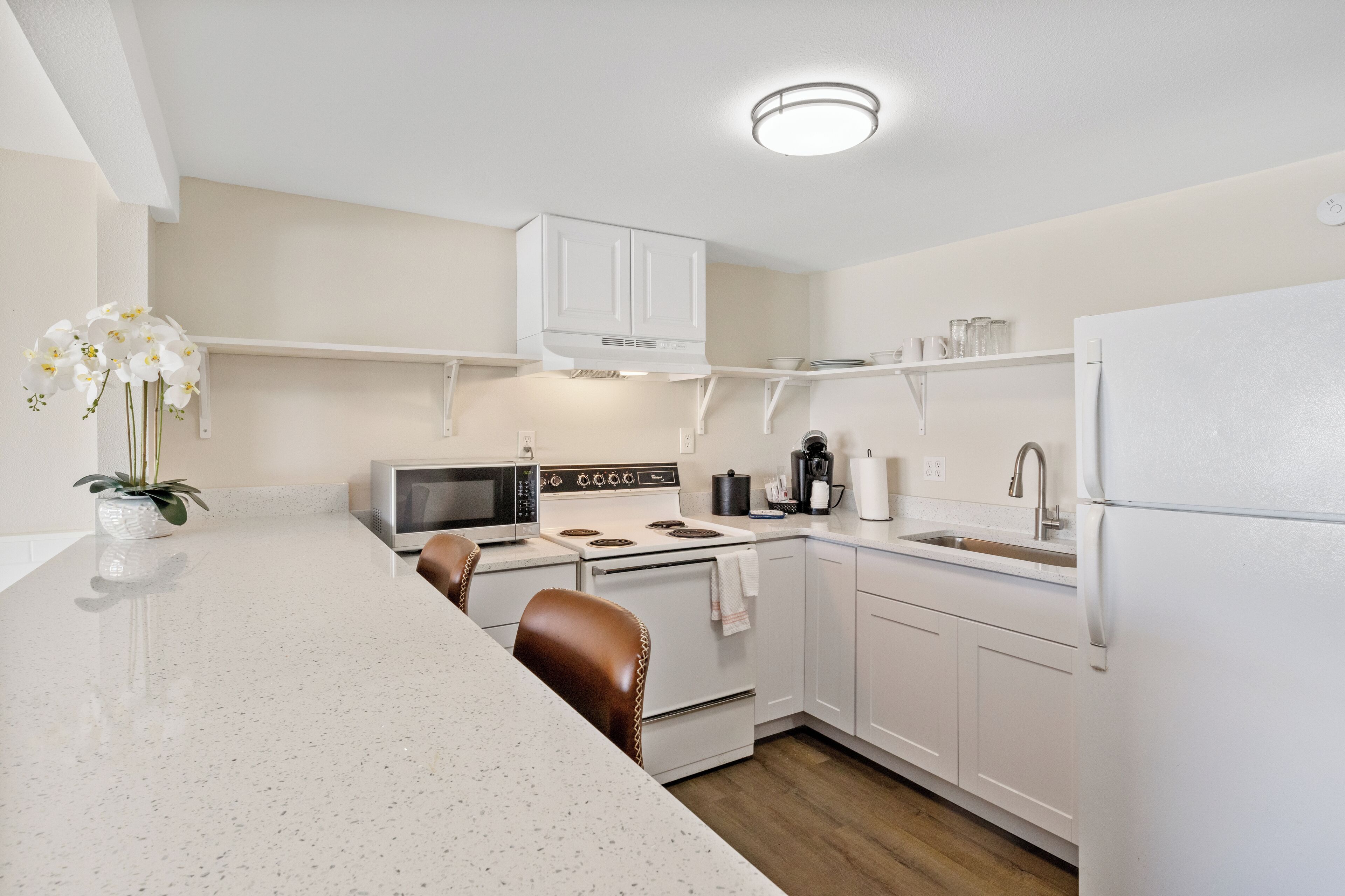 A modern kitchen with white cabinetry, a stainless steel refrigerator, a microwave, stove, and a sink.