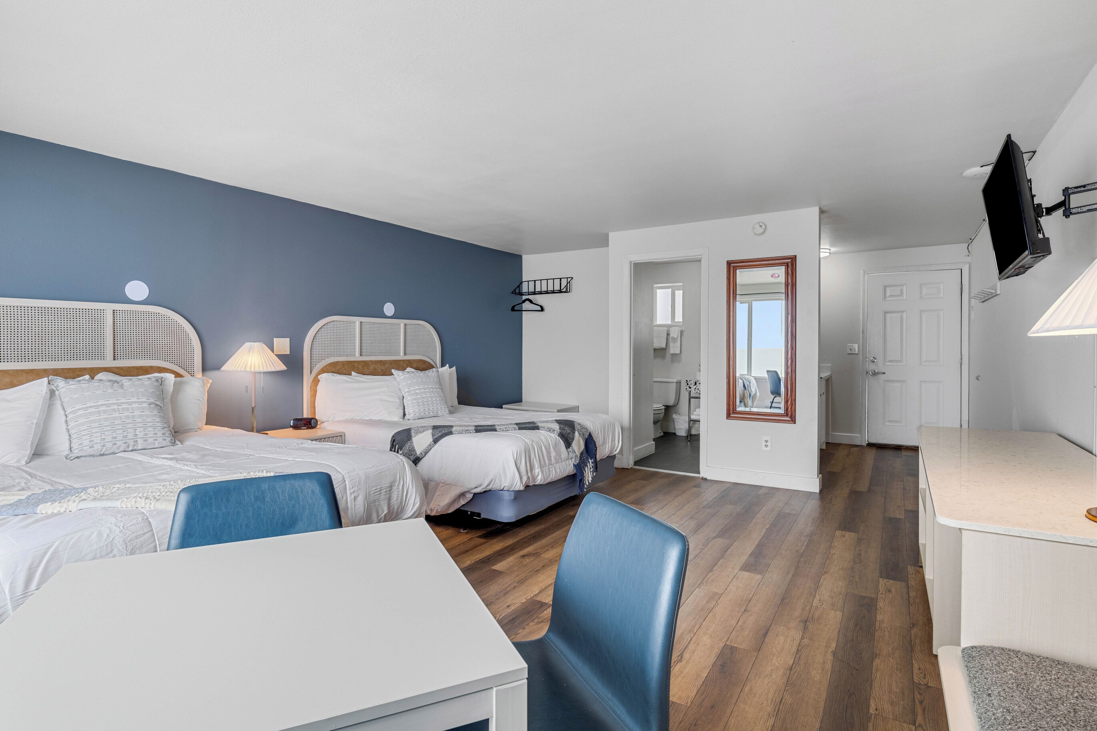 A hotel room with two beds, a desk, a chair, a TV, and a bathroom visible through an open door.