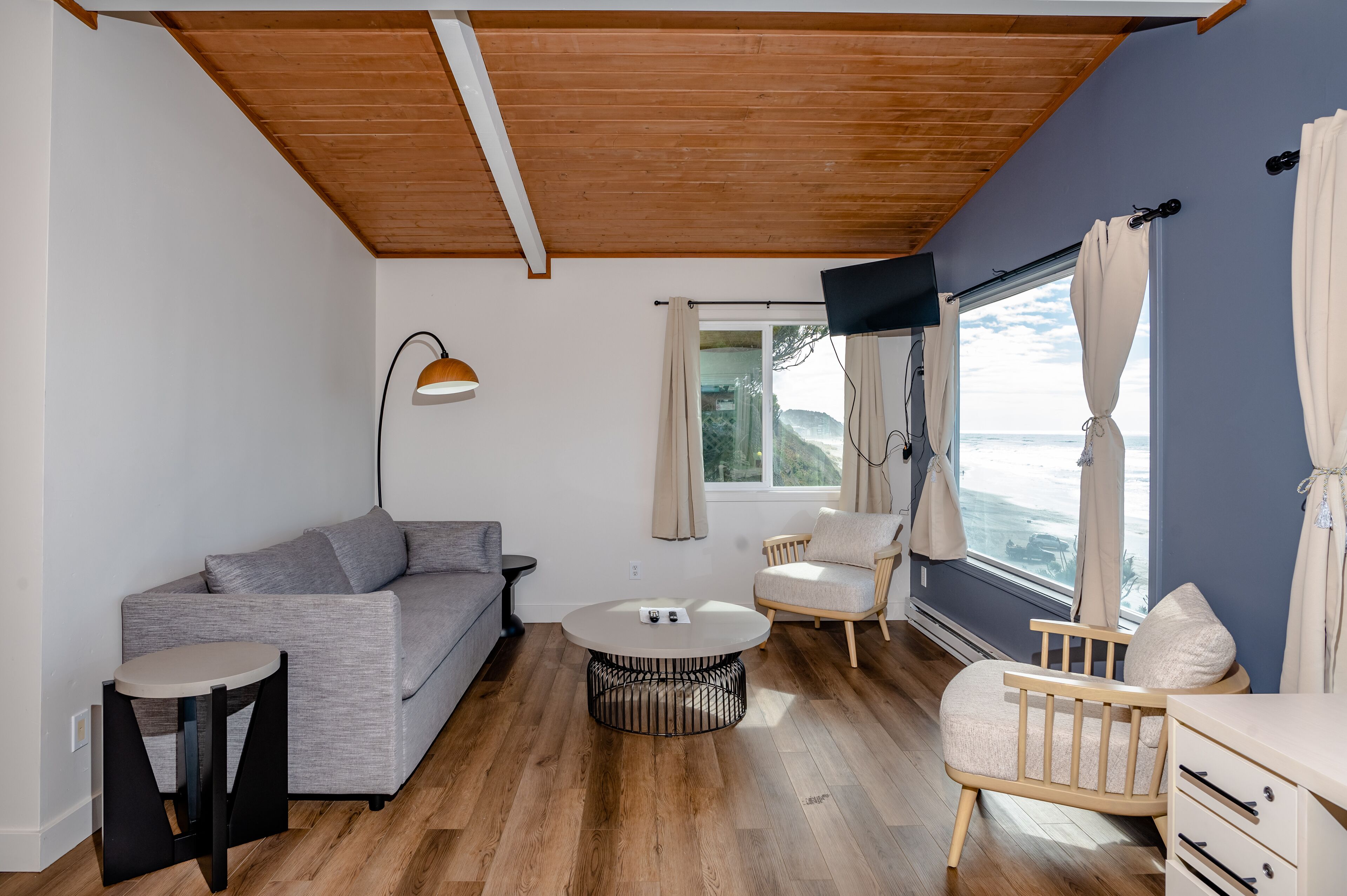 A modern living room with a grey sofa, a round coffee table, a wooden chair, and a crib.