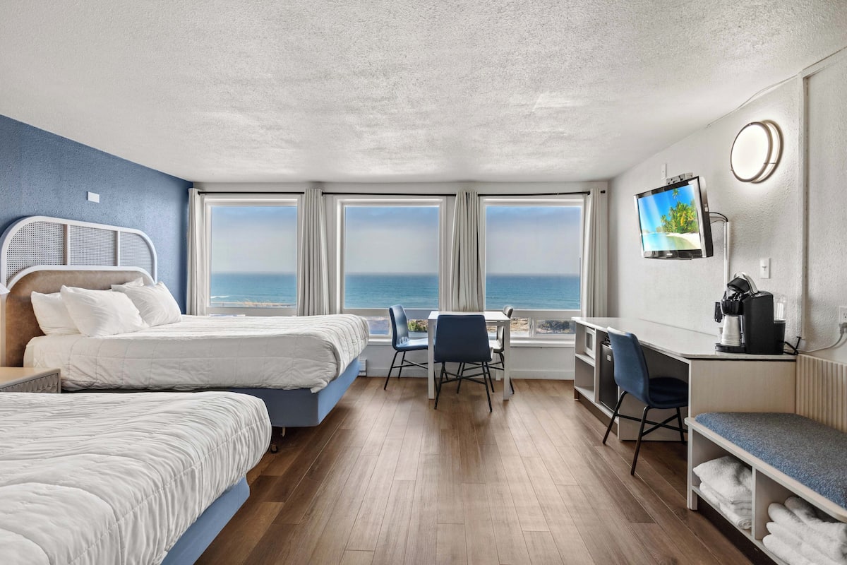 Een hotelkamer met twee bedden, een bureau, een stoel, een televisie en uitzicht op de oceaan.