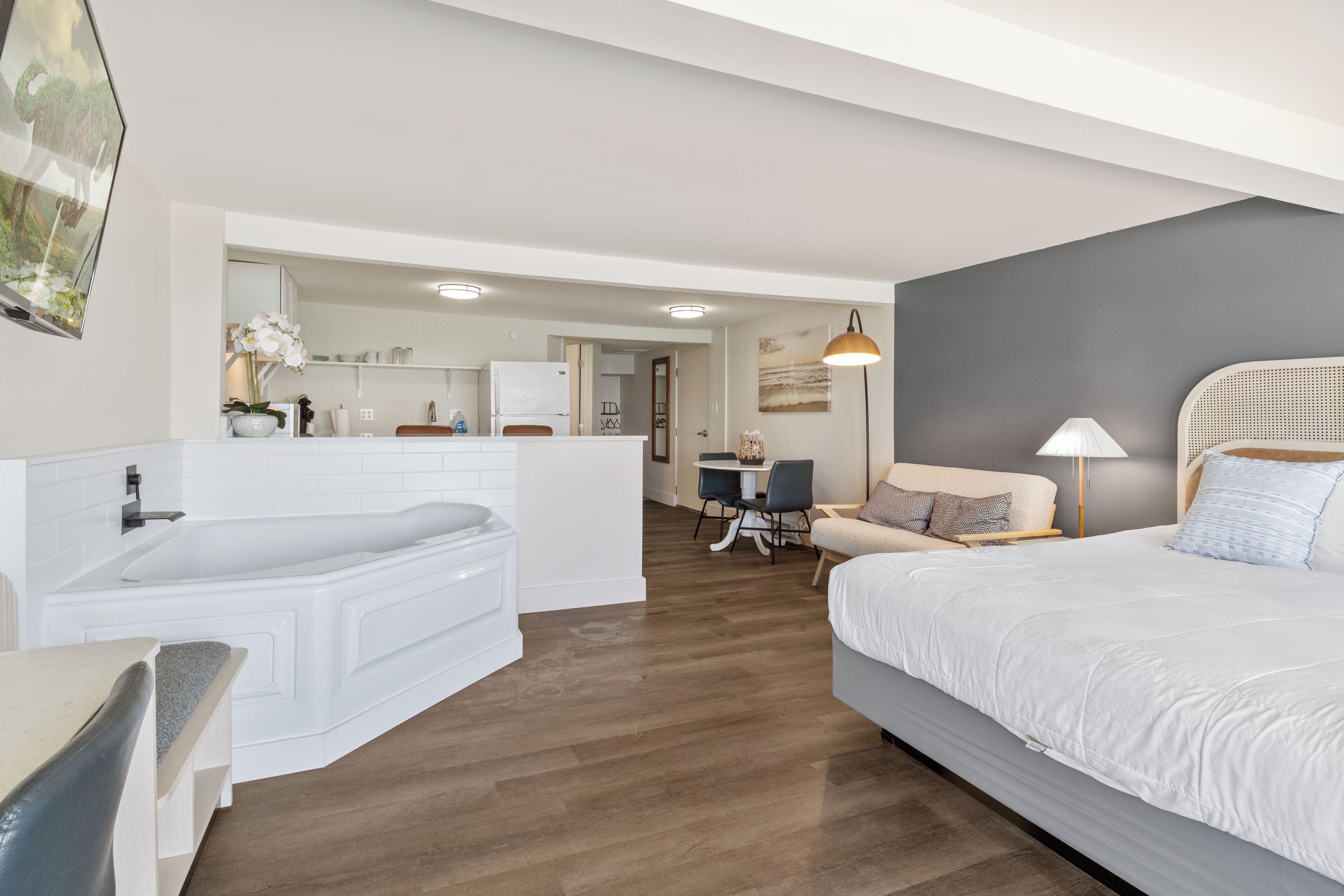 A modern hotel room with a large bed, a separate bathroom with a bathtub, a dining area, and a view of the city.