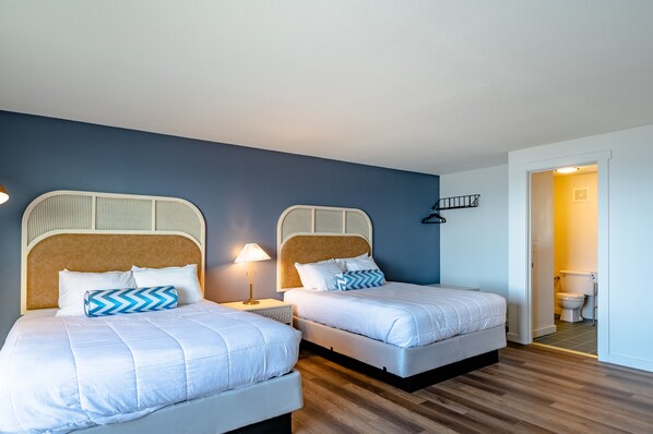 A hotel room with two beds, a wooden floor, a blue wall, and a white door leading to a bathroom. - Seagull Beachfront Inn (Lincoln City)