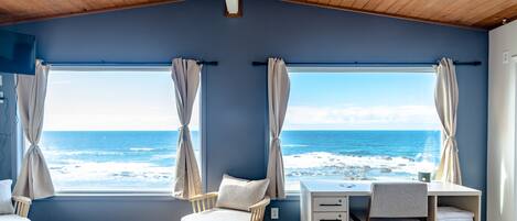 A room with a view of the ocean, a wooden ceiling, a desk, and a chair.